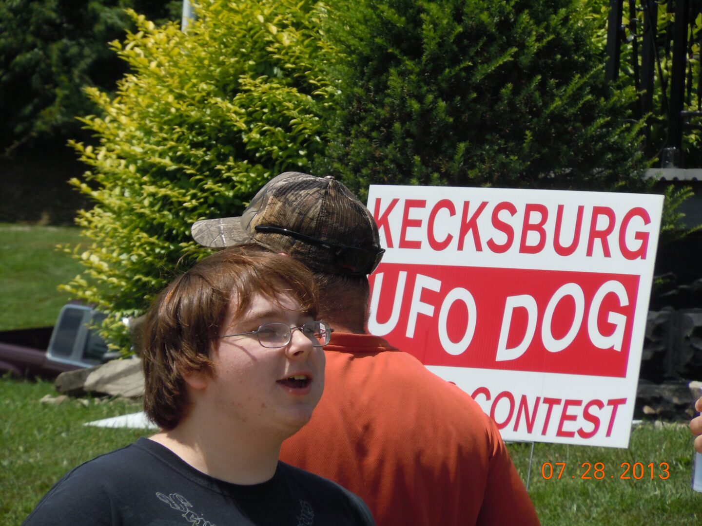 Two people standing next to a sign that says " kecksburg ufo dog contest ".